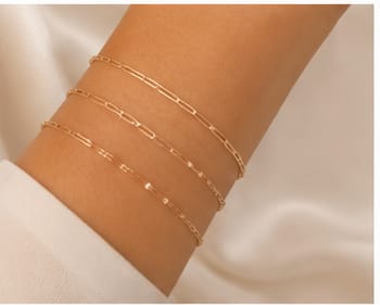 Three delicate gold permanent bracelets on a wrist